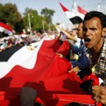 Opponents of President Morsi shout slogans while holding a giant Egyptian flag outside the presidential palace in Cairo. (AFP)