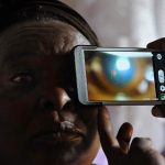 A technician scans the eye of Mary Wambui at her home with a smartphone application as she takes part in an ophthalmological study and examination. (Pic: AFP)