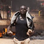 A protester carries rocks in front of a burning roadblock in Ouagadougou, capital of Burkina Faso. (Pic: AFP)