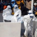 Rescued migrants watch as the body of person who died after a fishing boat carrying migrants capsized off the Libyan coast, is brought ashore along with 23 others. (Pic: AFP)